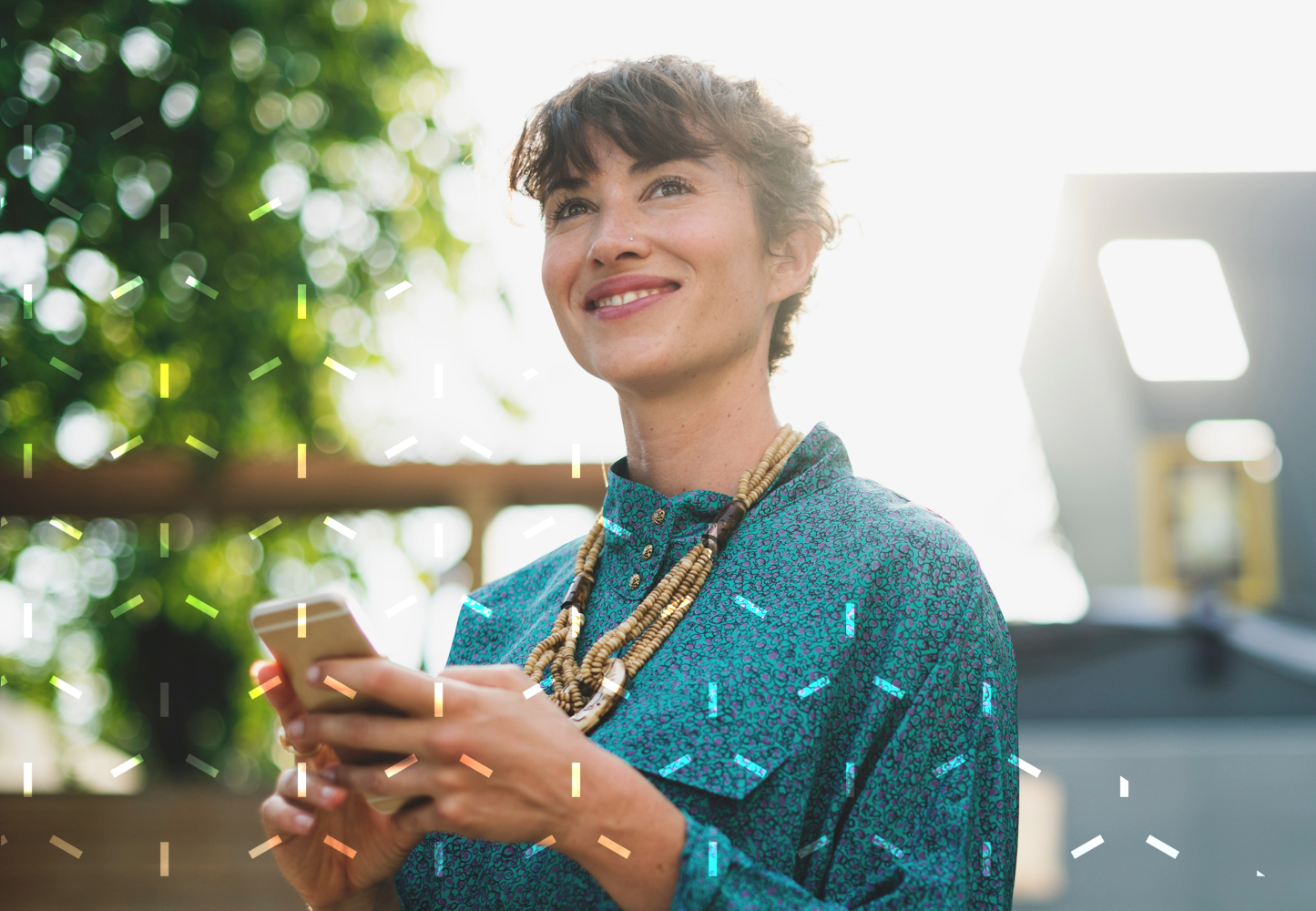 A woman looks up and smiles while holding a smartphone.