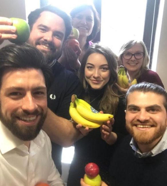 A group of people hold up fruit and smile