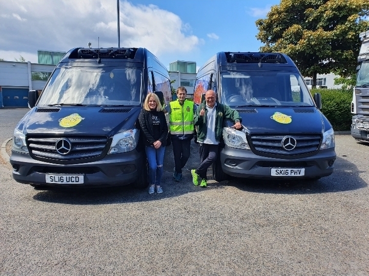 3 people, a younger man with an older man and woman smiling standing in front of 2 Charles Stamper vans. The younger man is wearing high-vis jacket and both men appear to be wearing clothes with the Charles Stamper logo on