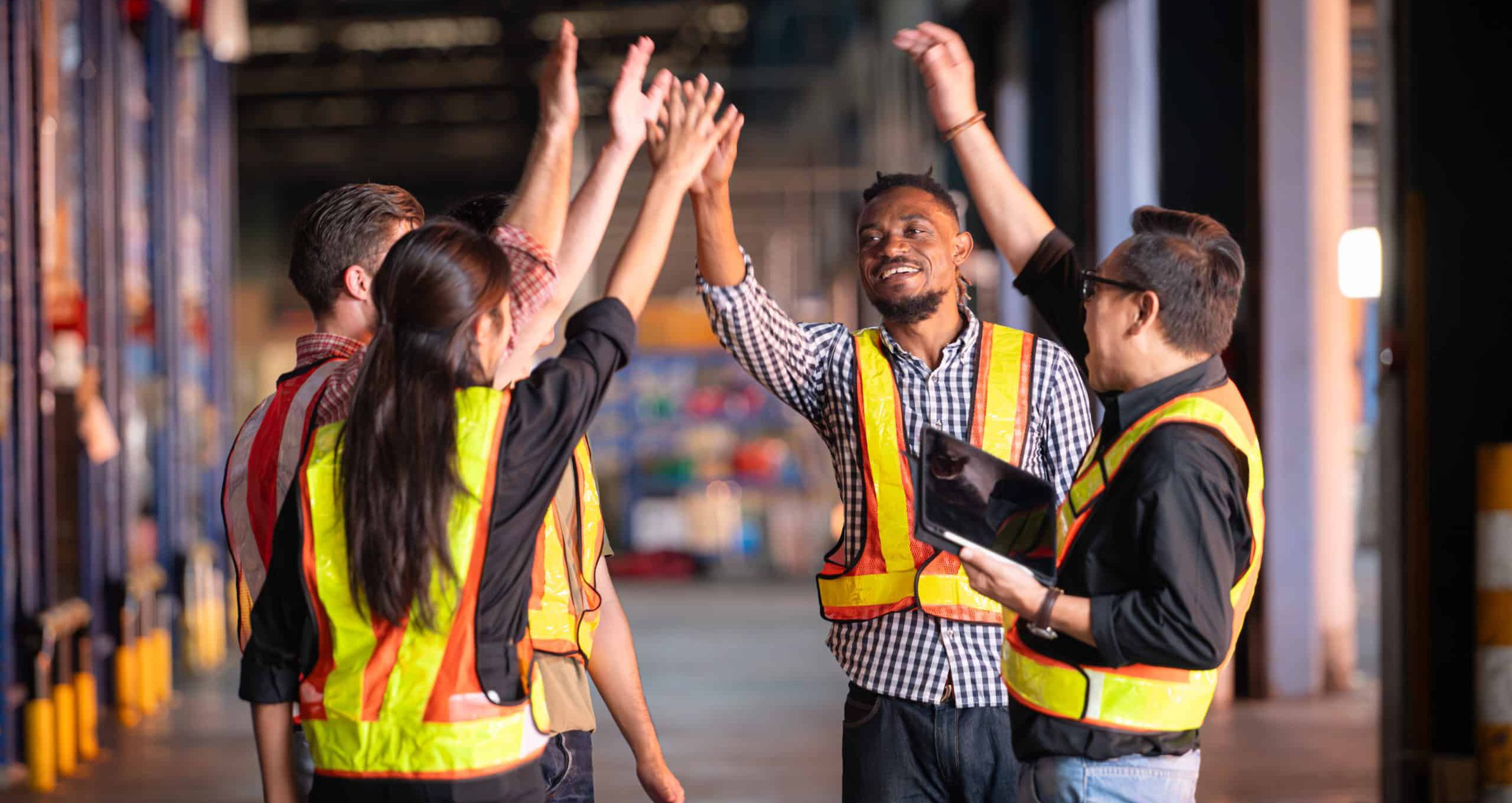 Group of drivers in a warehouse celebating a success by raising their hands