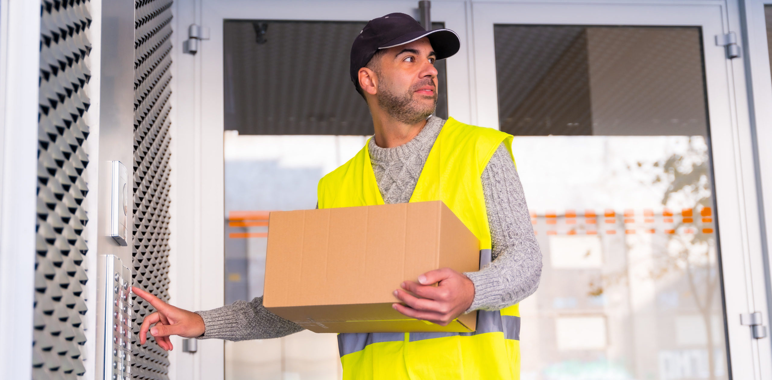 Delivery driver in high vis jacket, holding parcel, ringing doorbell and waiting at the door