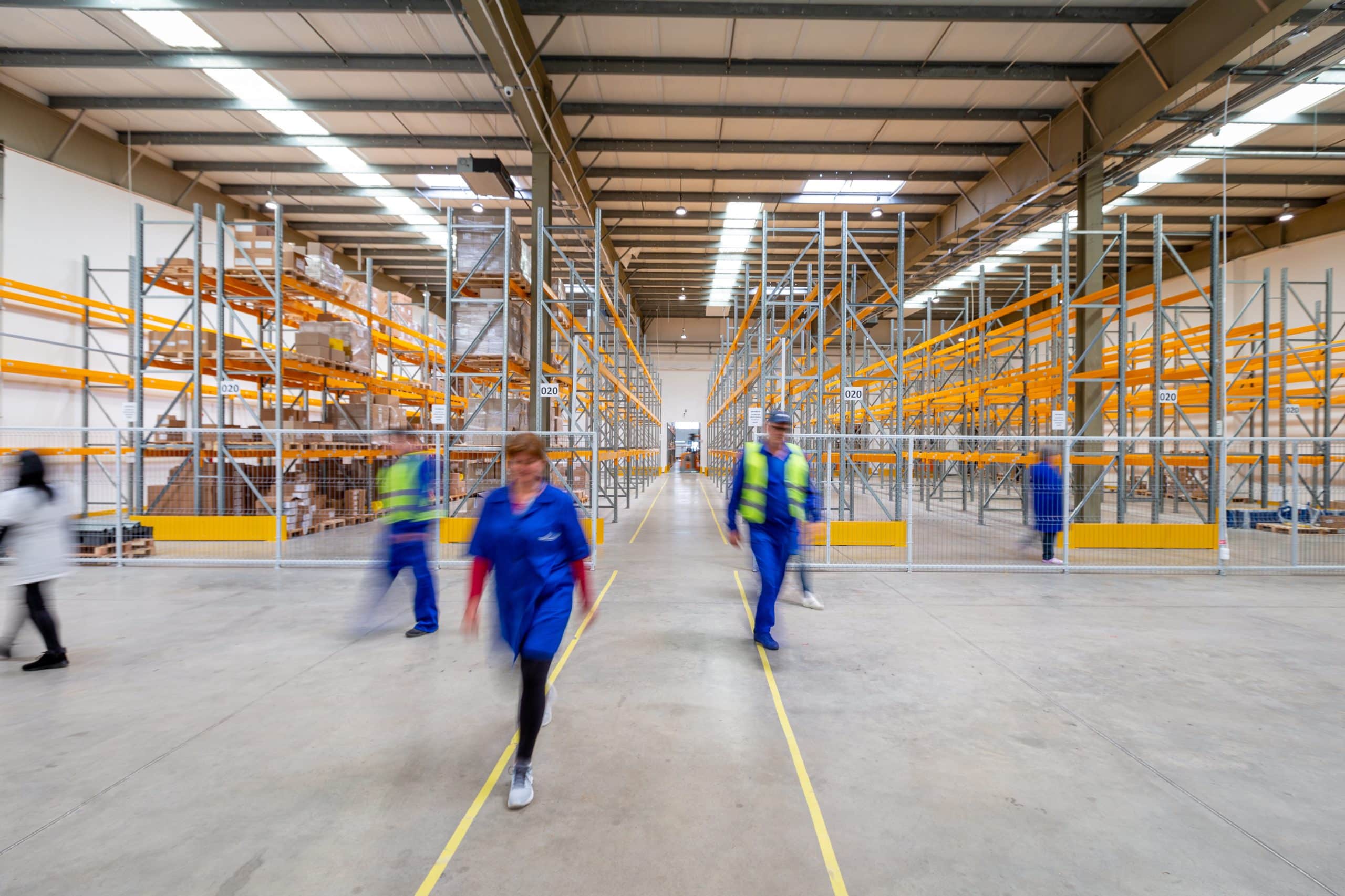 Generic warehouse with warehousers workers dressed in blue, workers are blurred to emulate fast pace and busyness