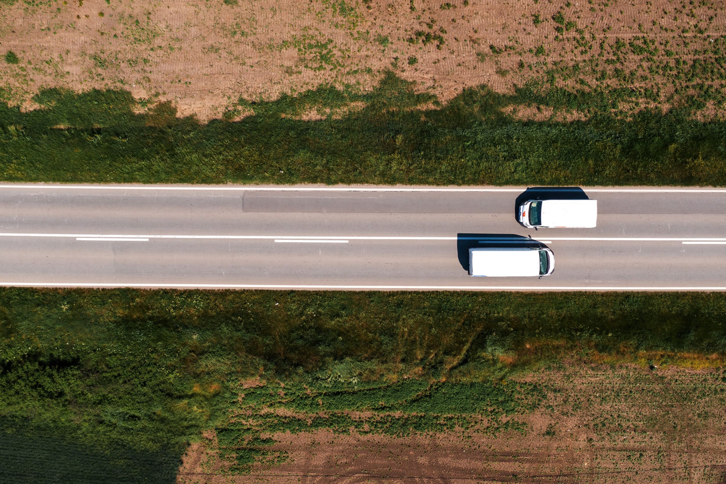 Aerial shot of two white van vehicles passing by each other on a road through countryside landscape on sunny summer day