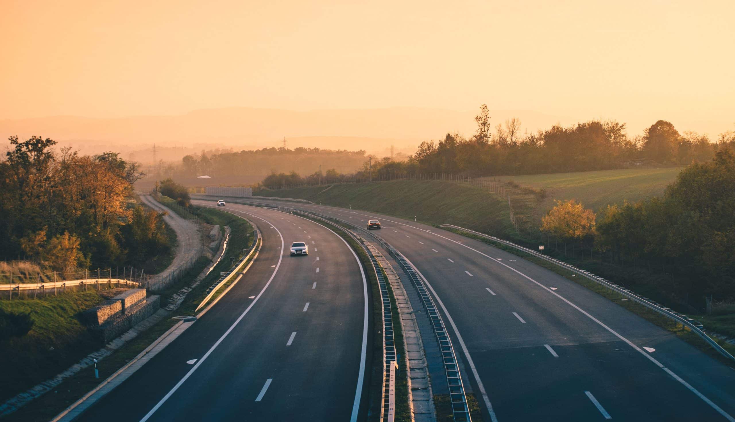 An aerial view of a truck on an empty highway with trees and hills in the background