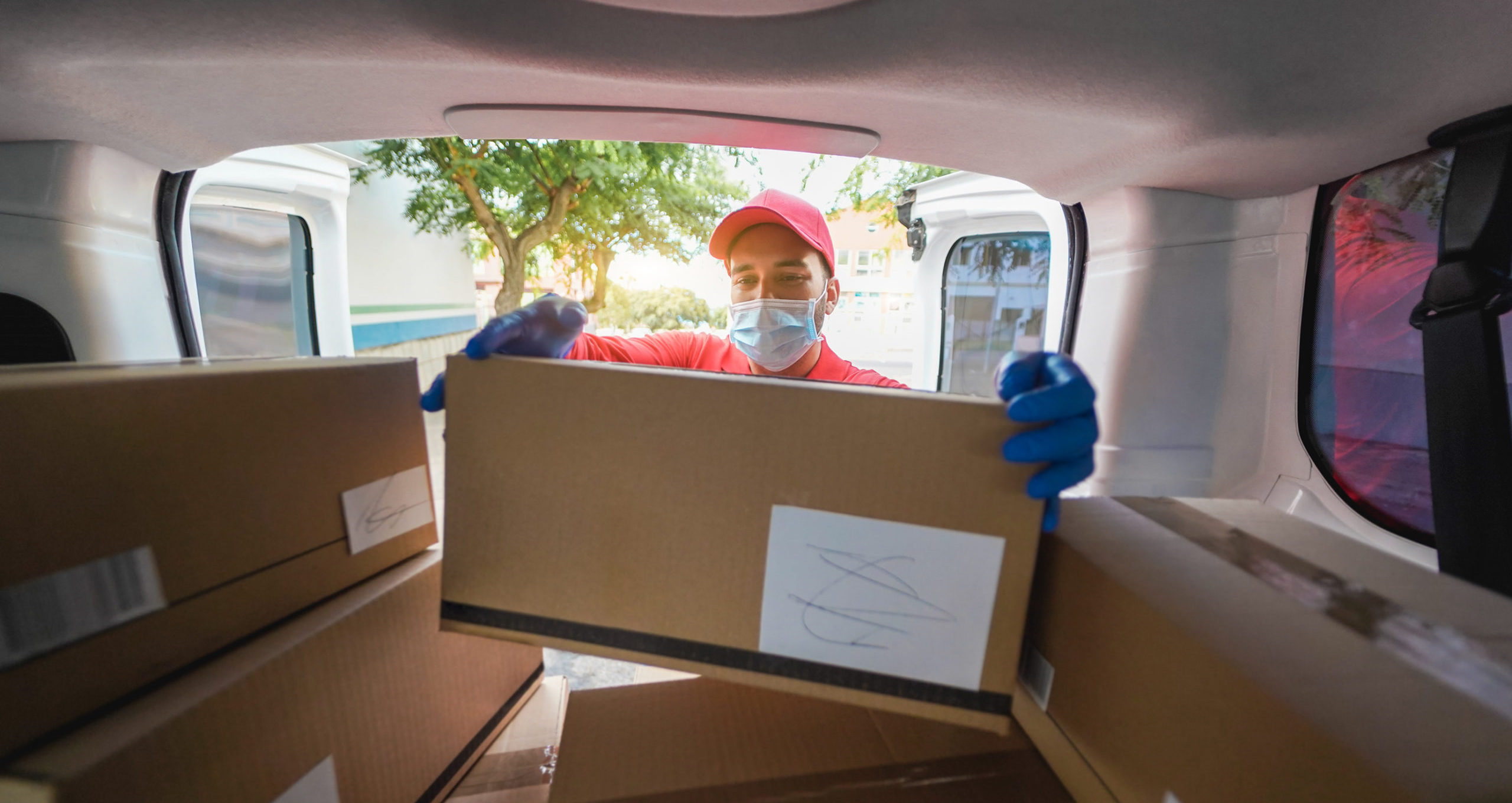 Courier man with safety mask holding cardboard box for delivery - Focus on face