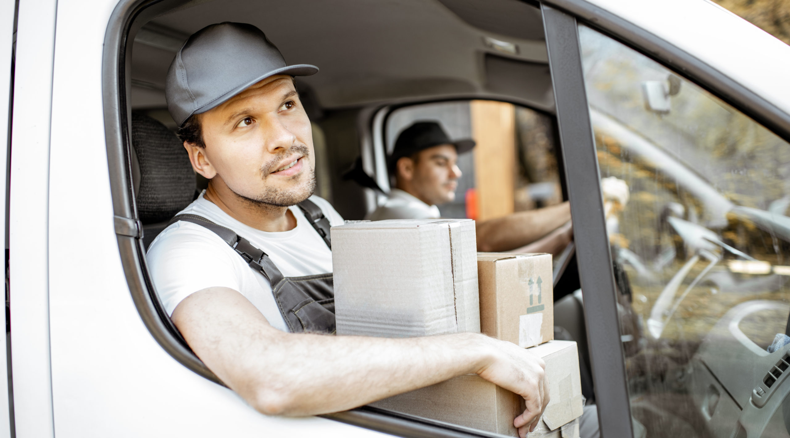 Two delivery drivers in delivery van, one holding boxes and looking out of window