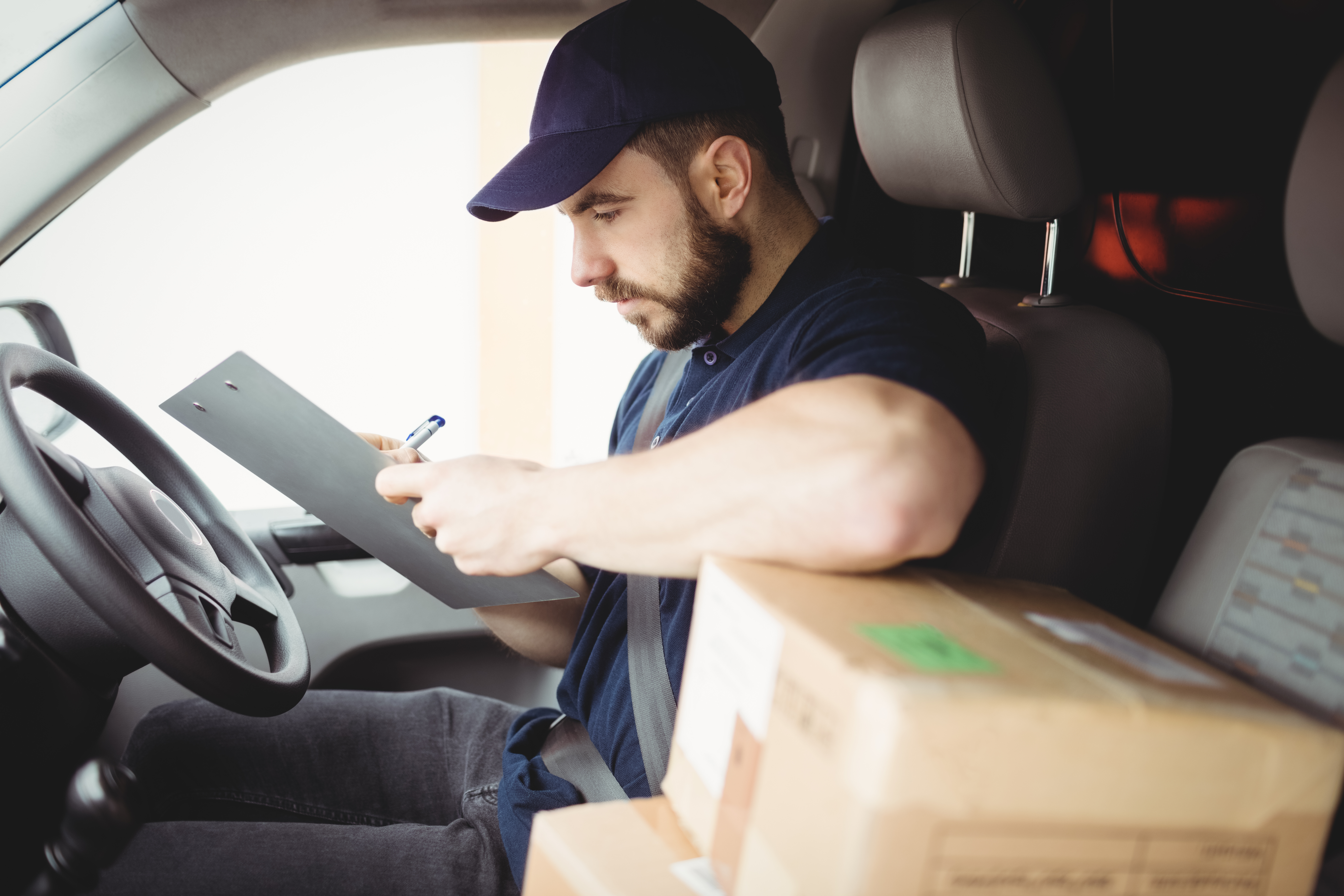 Delivery driver who isn't using routing software, being overwhlemed by orders on Black Friday. He is sitting in his van, signing of orders on a paper rota.