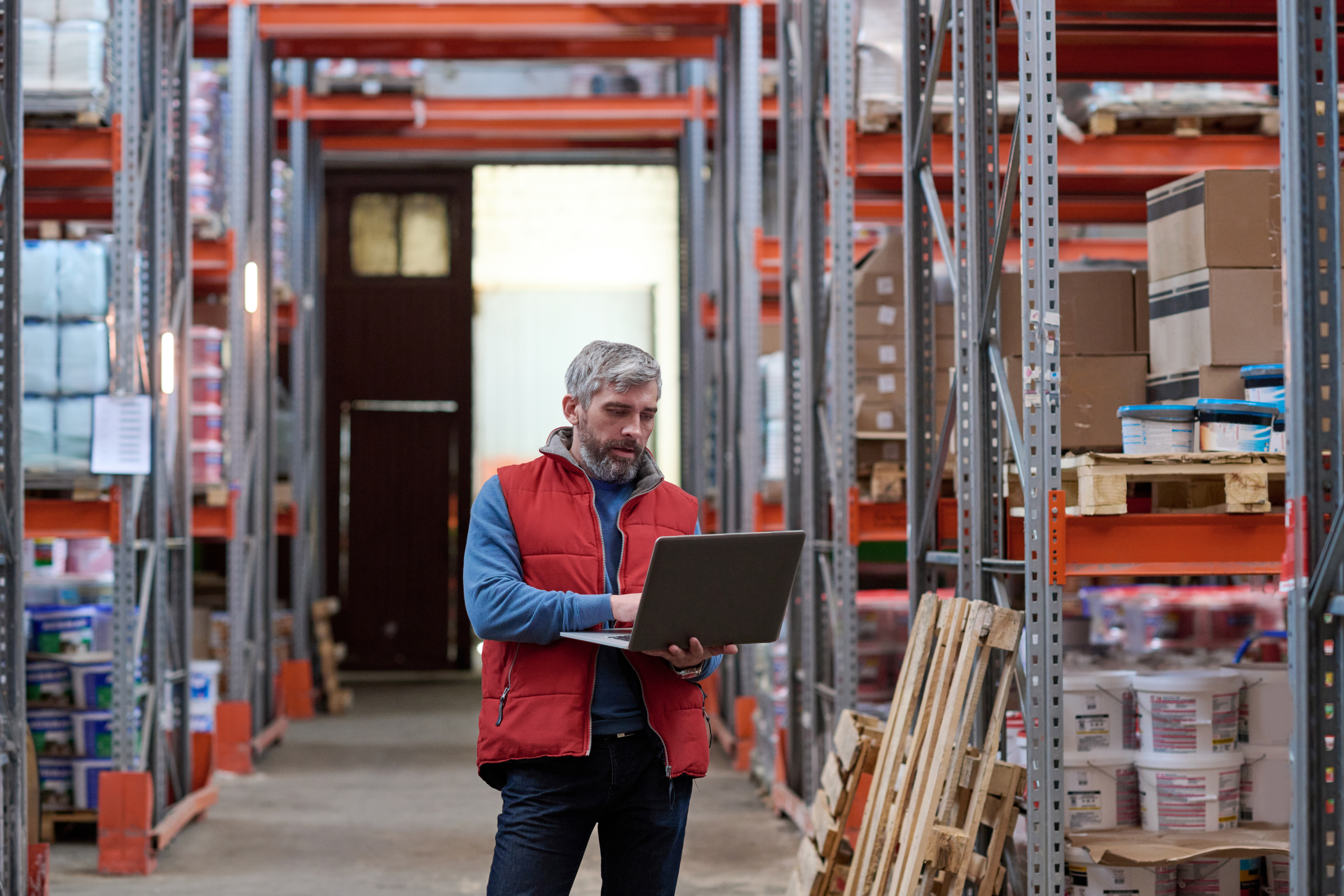 Warehouse manager using a laptop in a warehouse for his multi drop delivery route planning