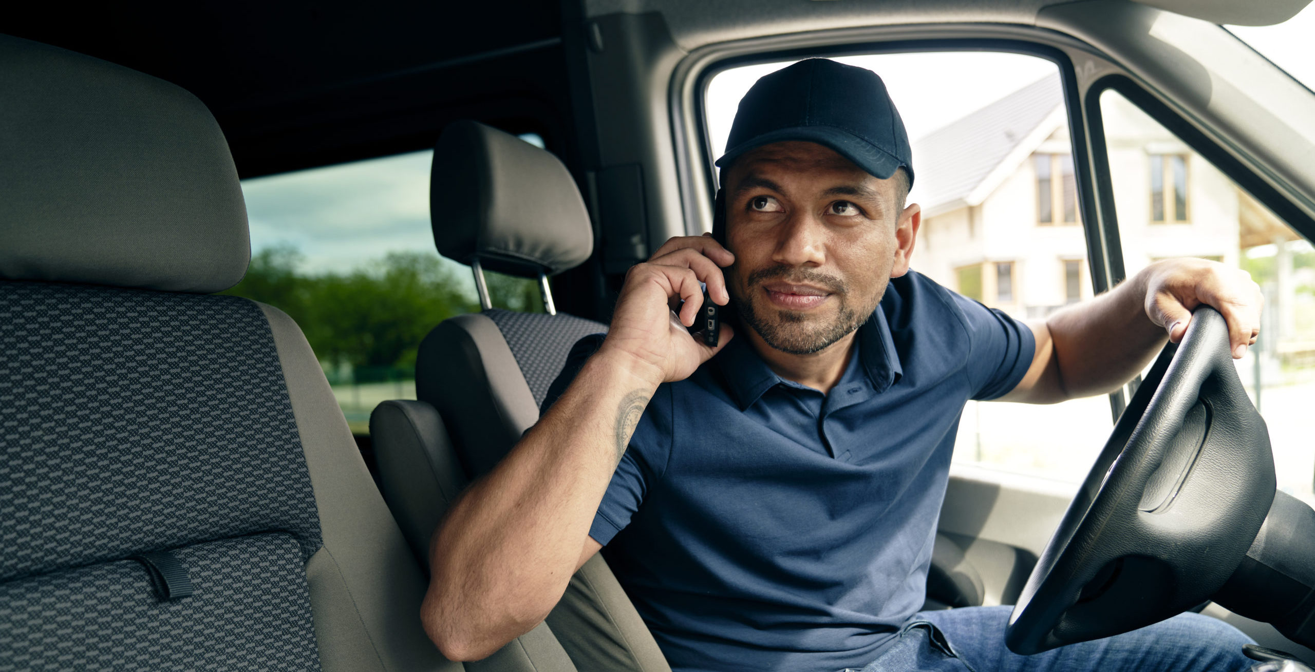 Delivery driver in van talking on phone and looking towards the camera out of window