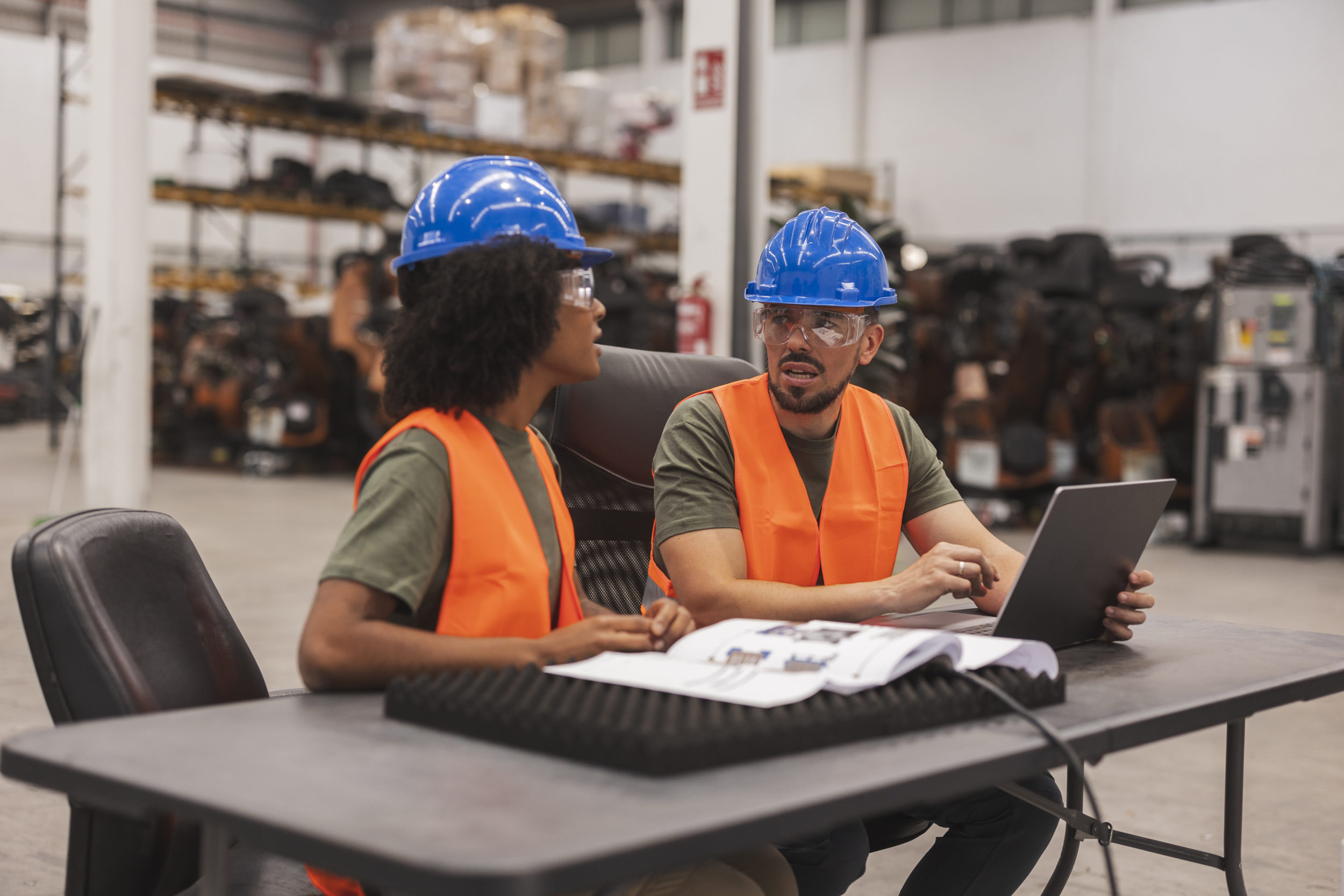 Two workers wearing high vis jackets and hard hats working on a computer