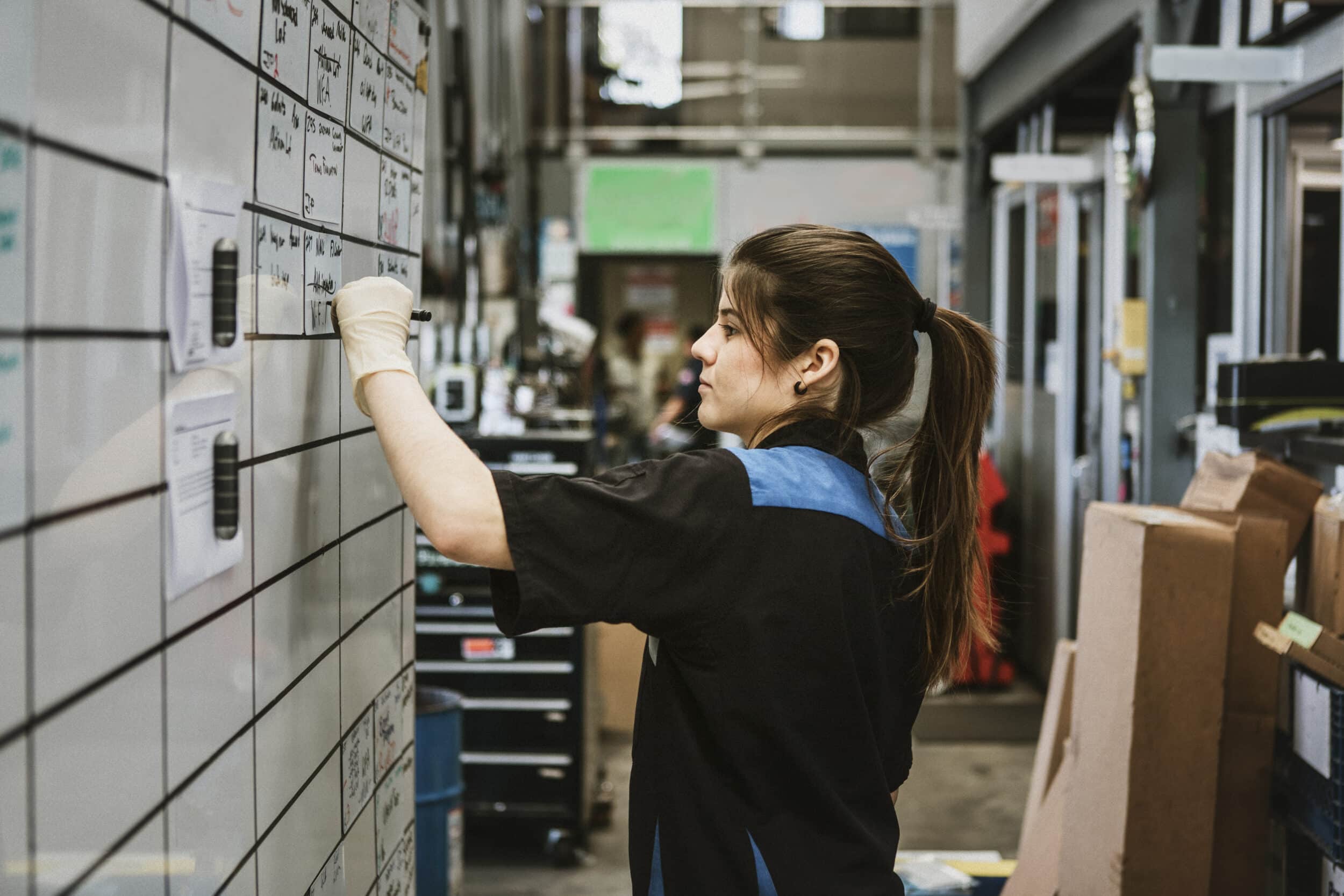Female warehouse employee writing on a large whiteboard schedule