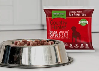 A silver bowl of dog food sits in front of a red packet of dog food.