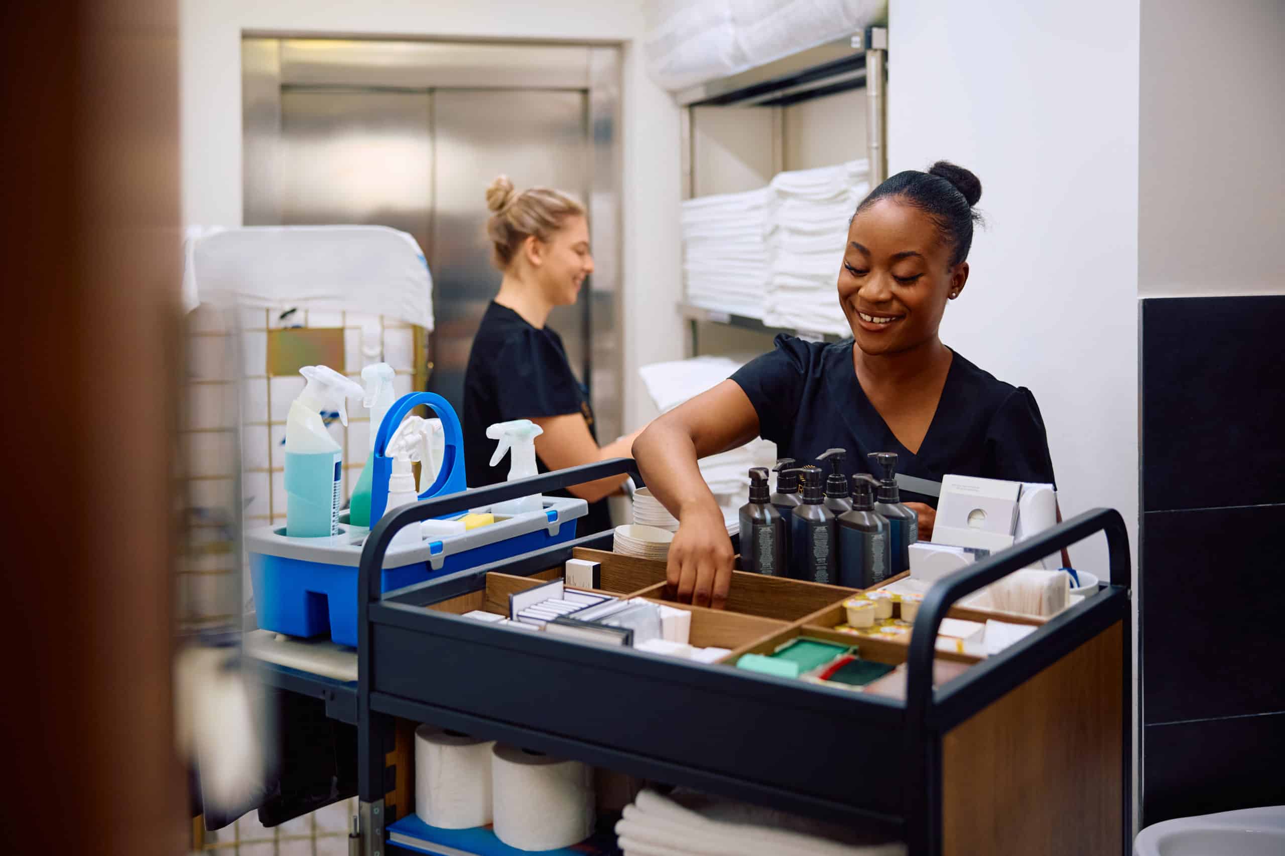 Smiling housekeeper restocking chamber maid's trolley while working in a hotel.