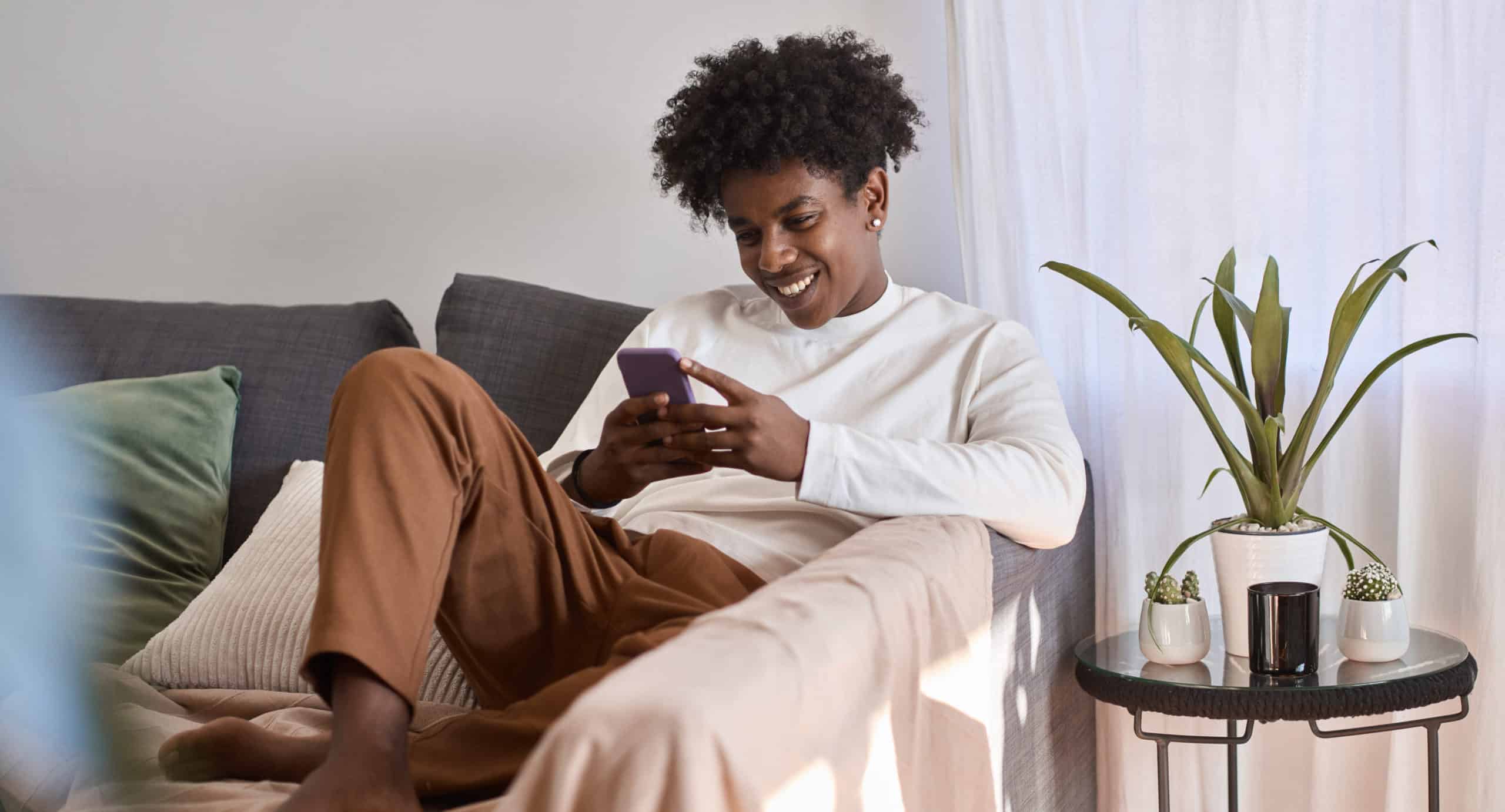 Smiling man sitting on sofa at home using his phone