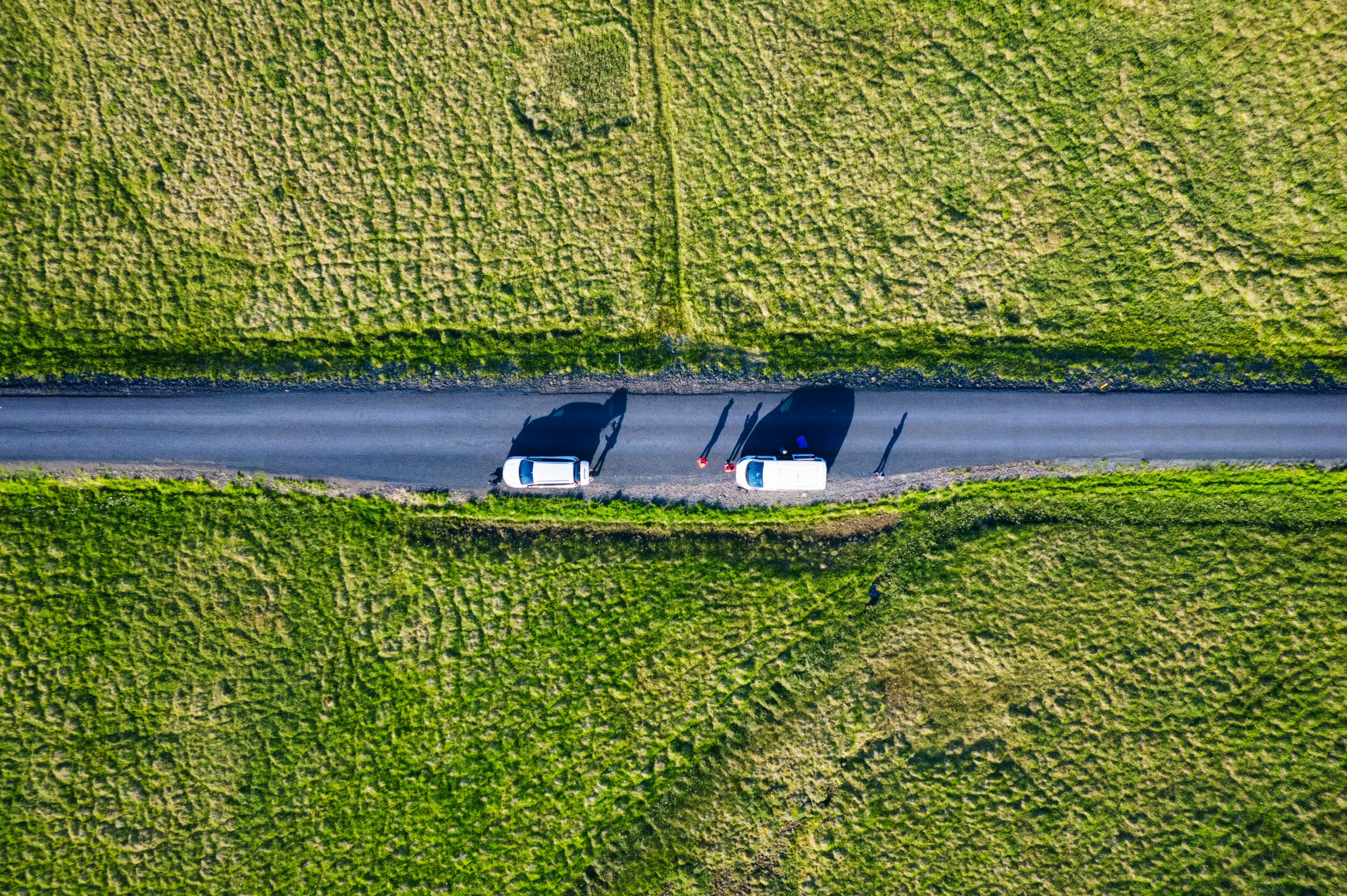 Aerial view of two white vans on a road, surrounded by green fields
