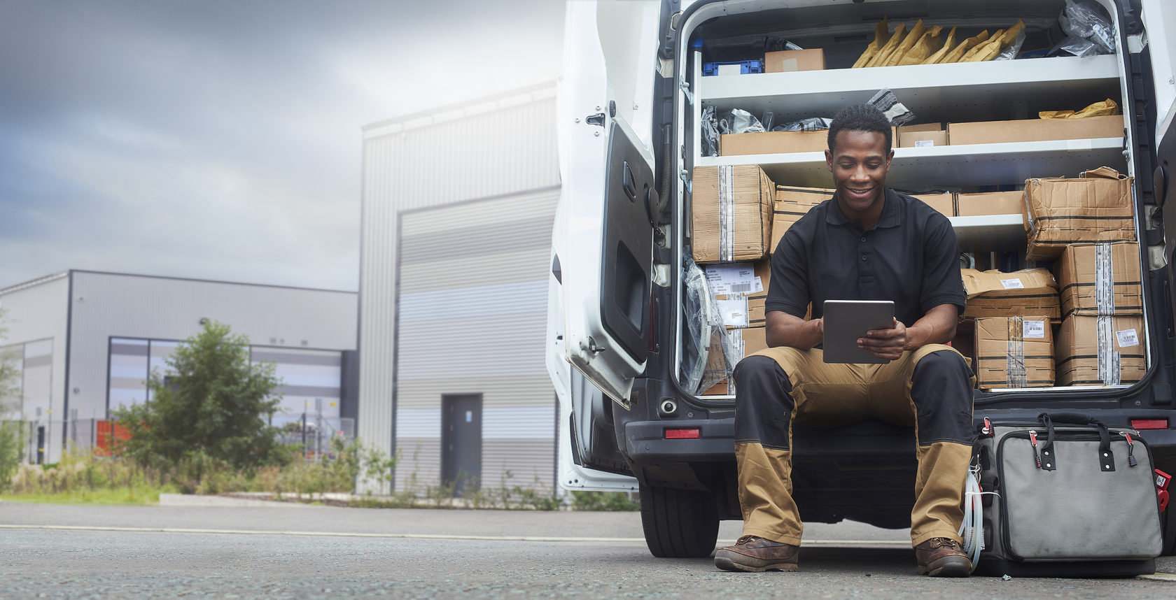 Man sitting at back of his delivery van looking at a tablet