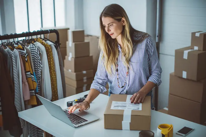 Retailer packing clothes for delivery and checking her laptop