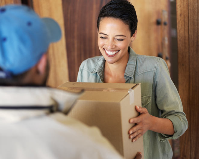 A smiling woman accepts a boxed parcel from a delivery man.