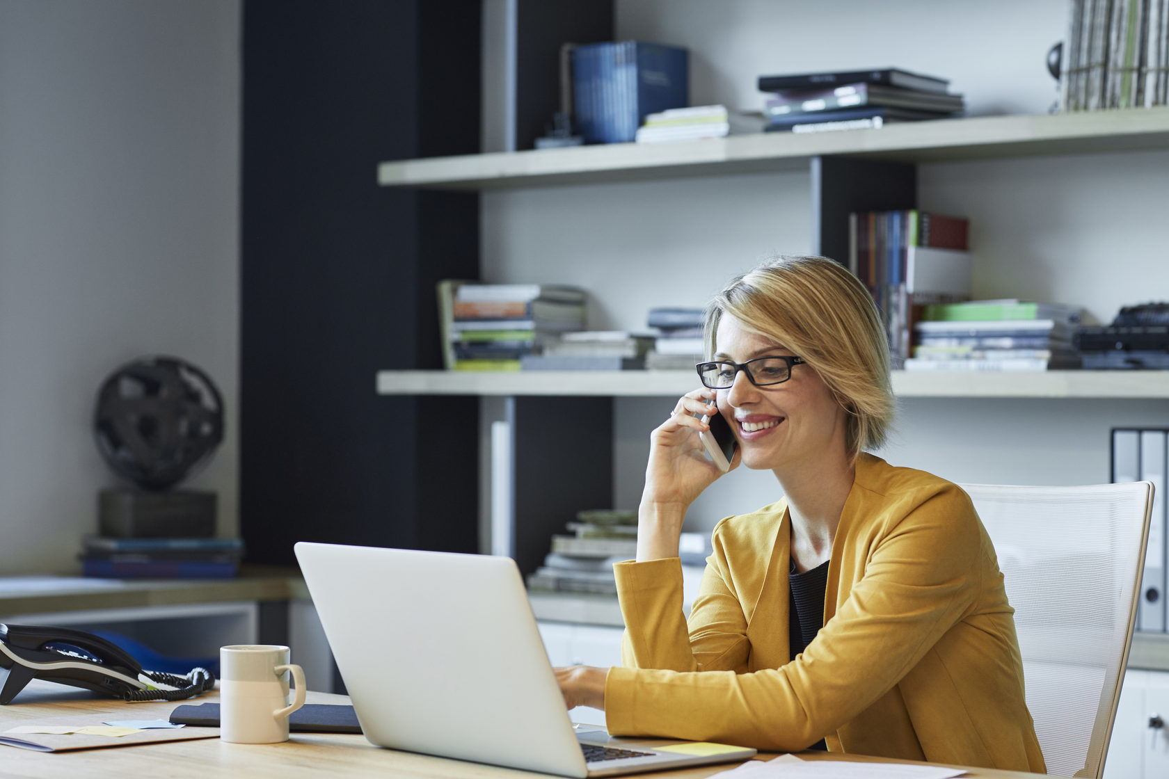 Woman sitting at her desk on the phone while pointing at laptop