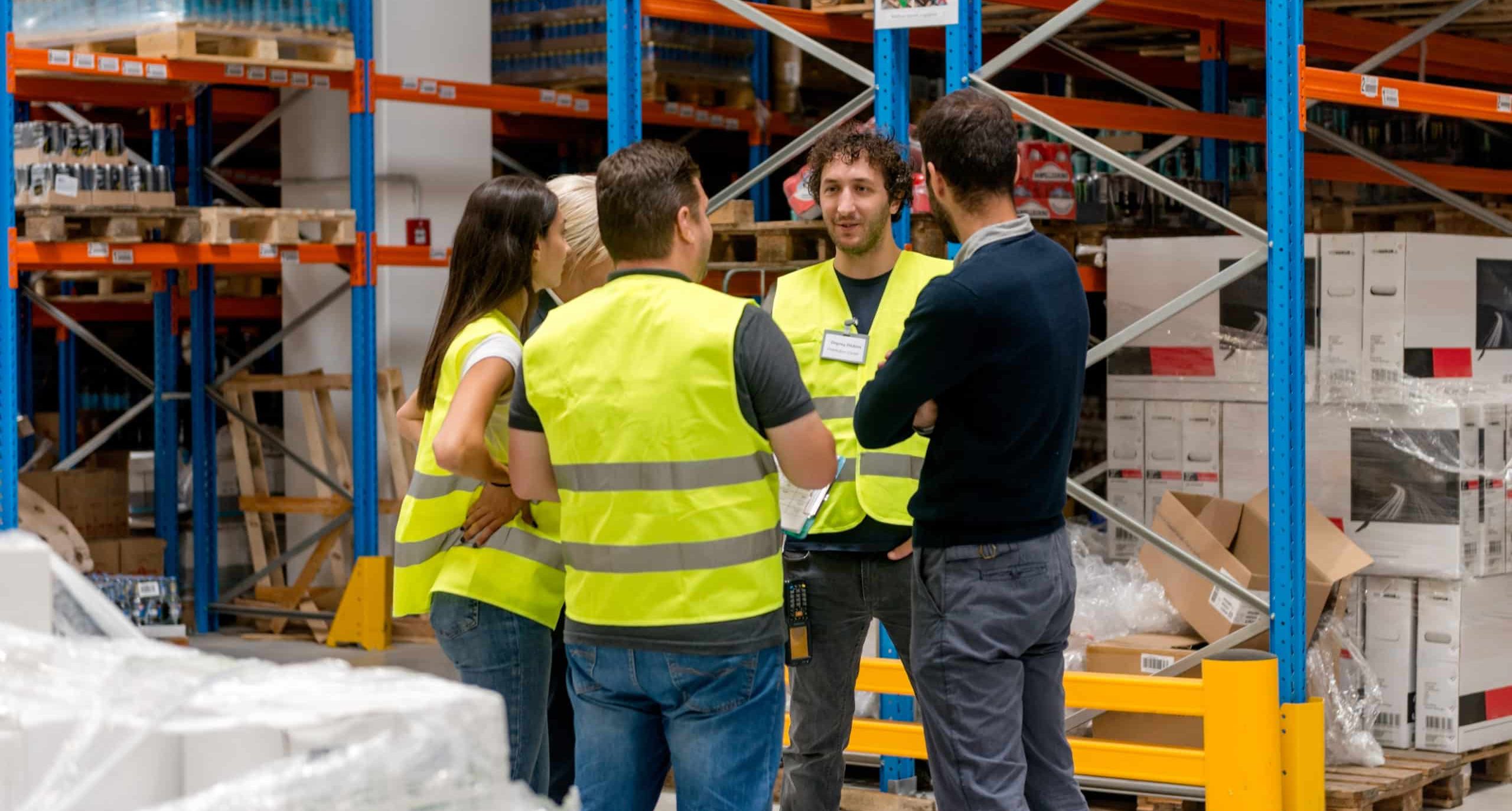 Group of warehouse workers in high-vis jackets meeting on warehouse floor