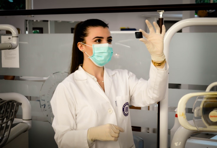 A scientist wearing a labcoat, gloves and a face mask holds up a small black object.