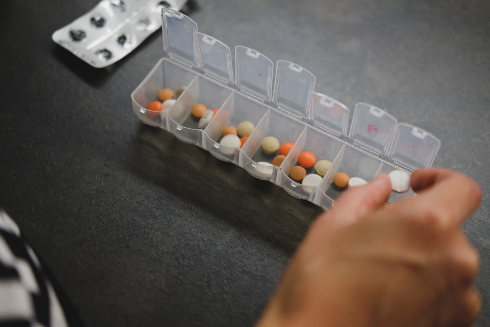 A hand hovers over a pill organiser.