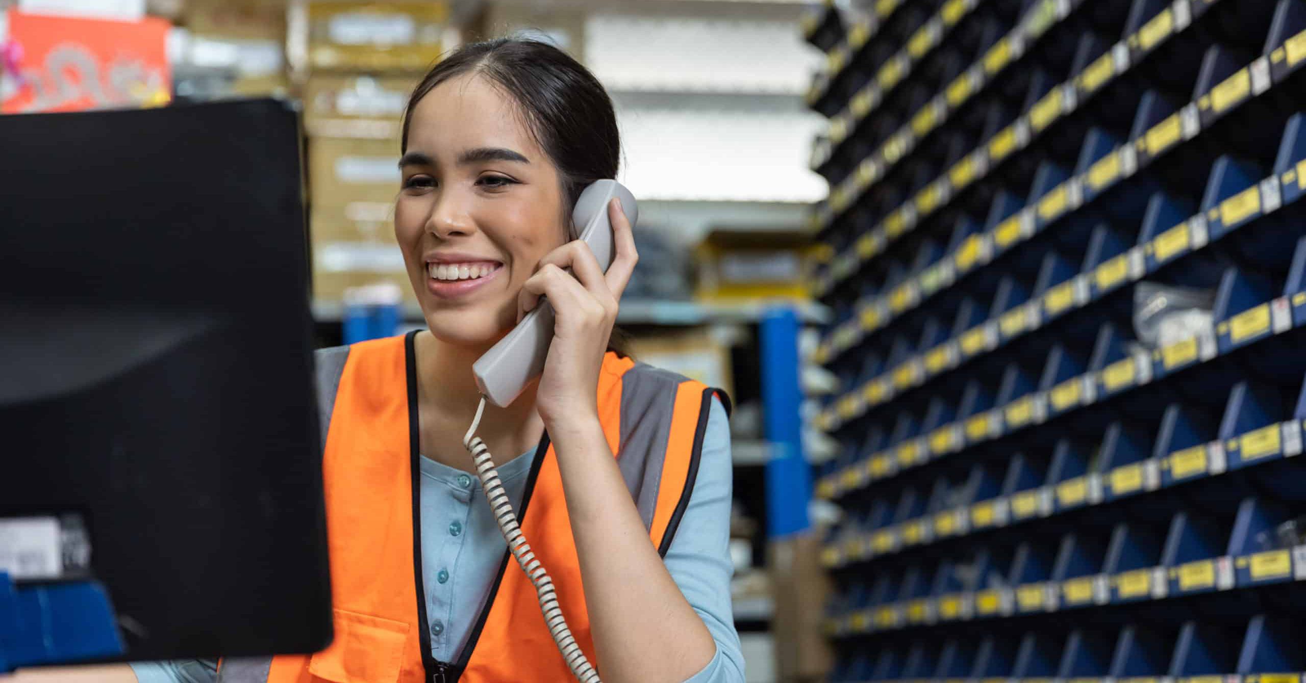 Woman in high vis jacket on phone looking happy whilst looking at computer screen