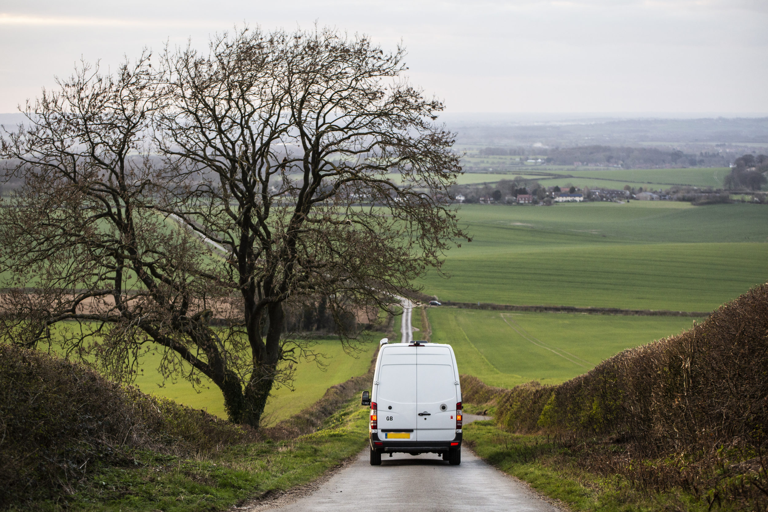 Rear view of a white delivery van driving down a country road