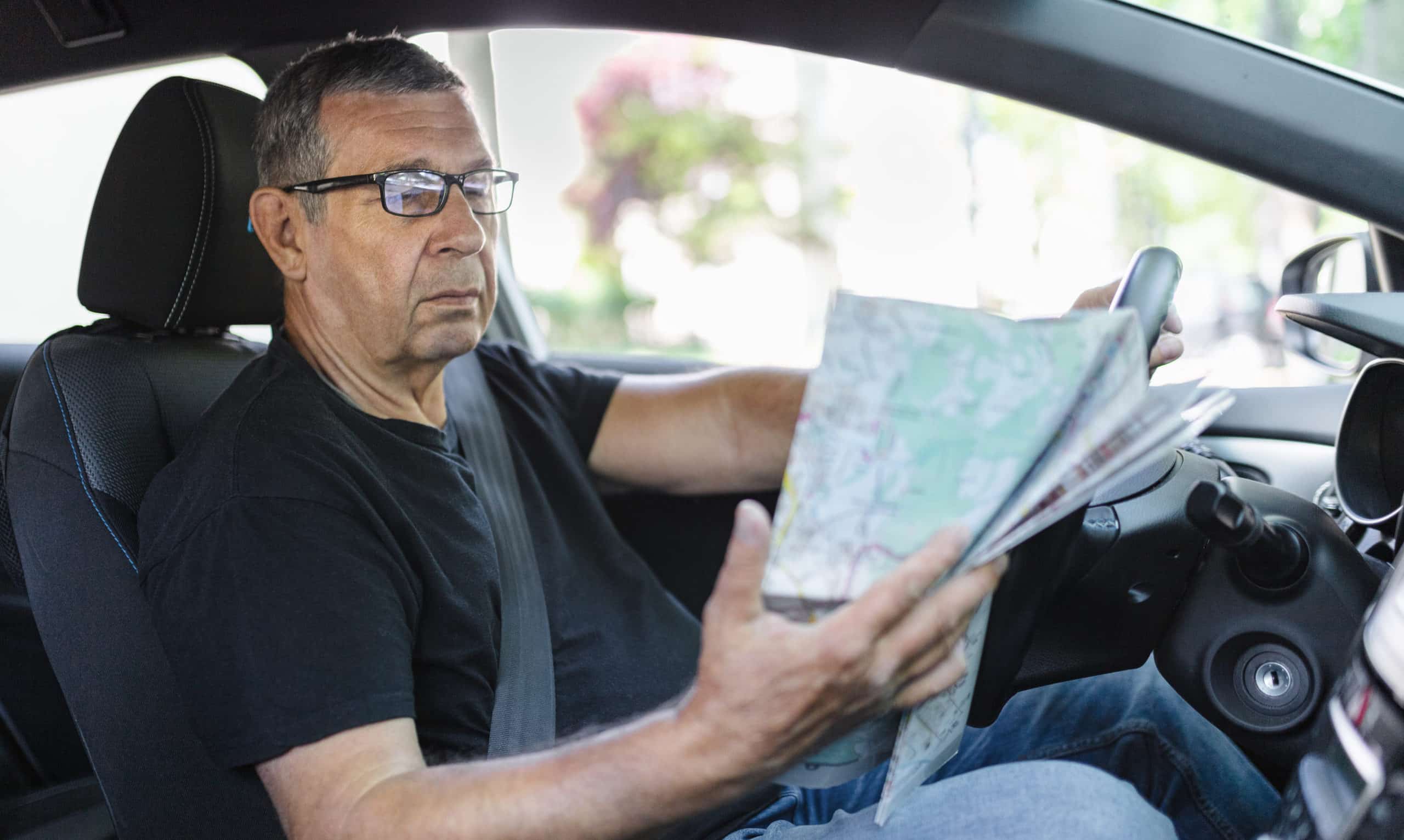 Driver behind the steering wheel of a car, looking at map for directions