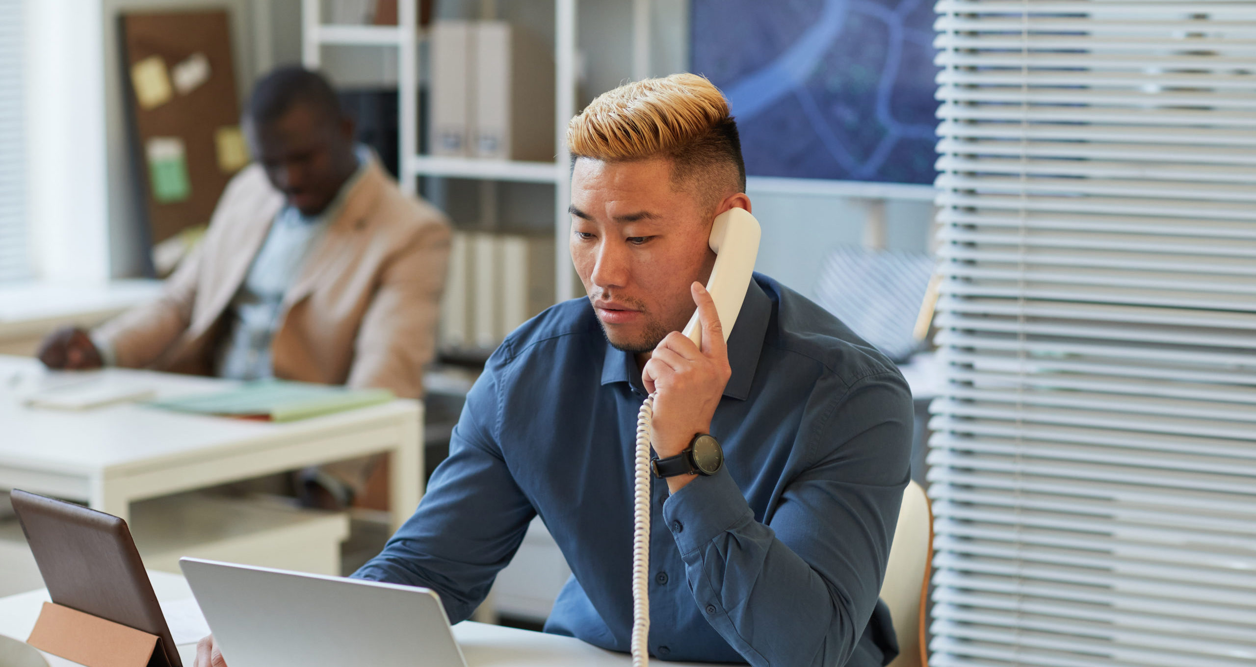 Man in office speaking on a phone, with a neutral expressions