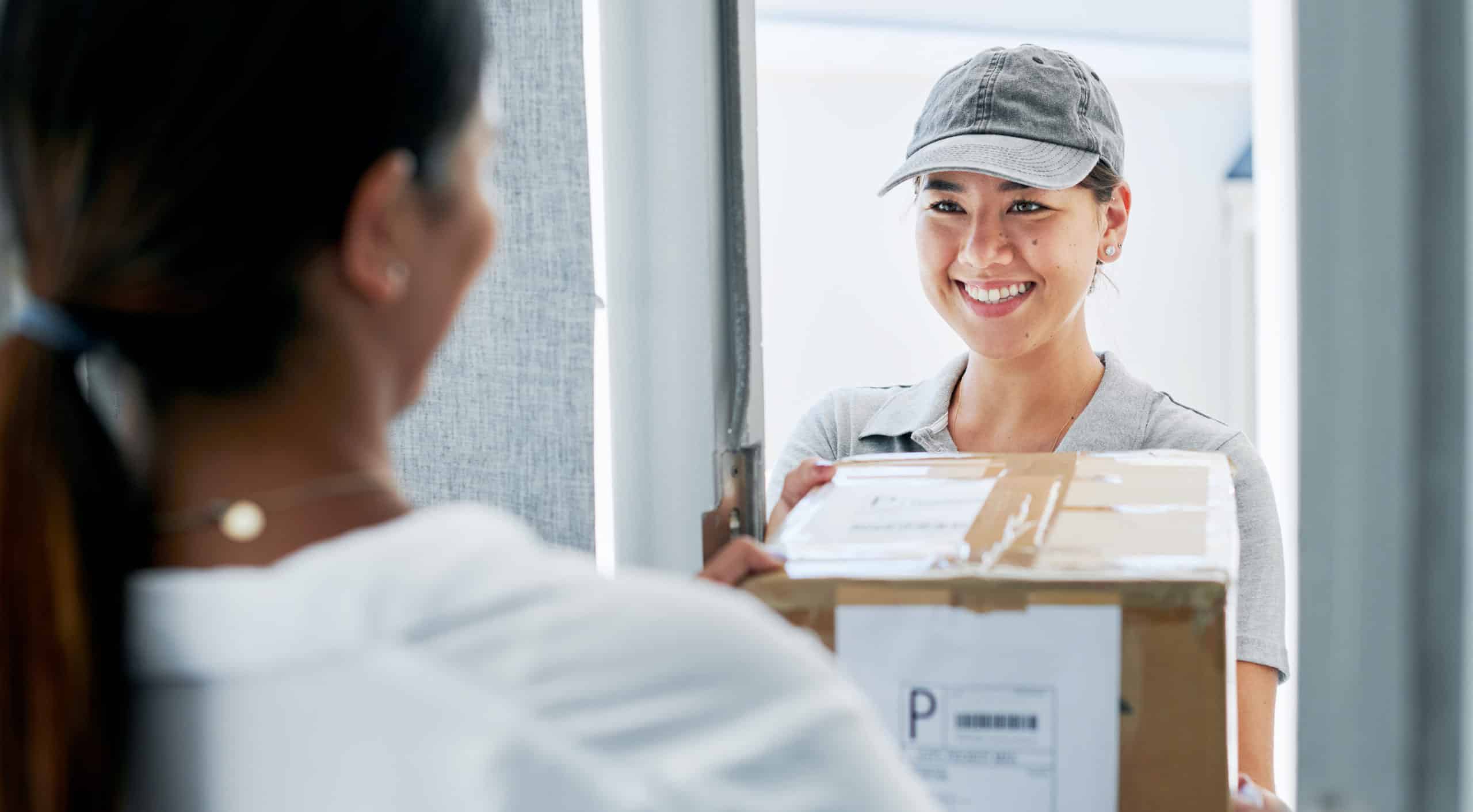 Shot of a female delivery driving standing and delivering a box to a customer at their home.