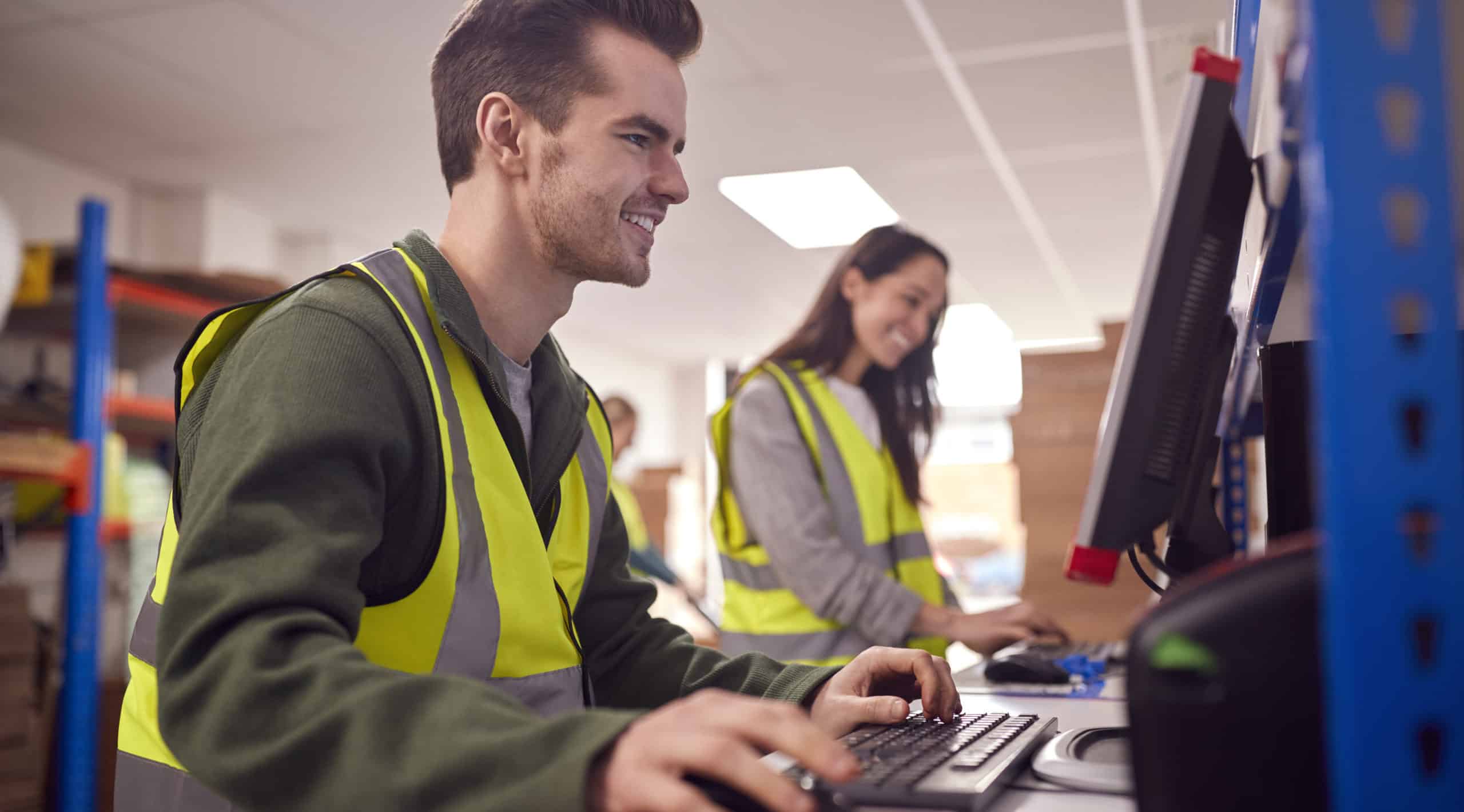 Staff In Busy Modern Warehouse Working On Computer Terminals