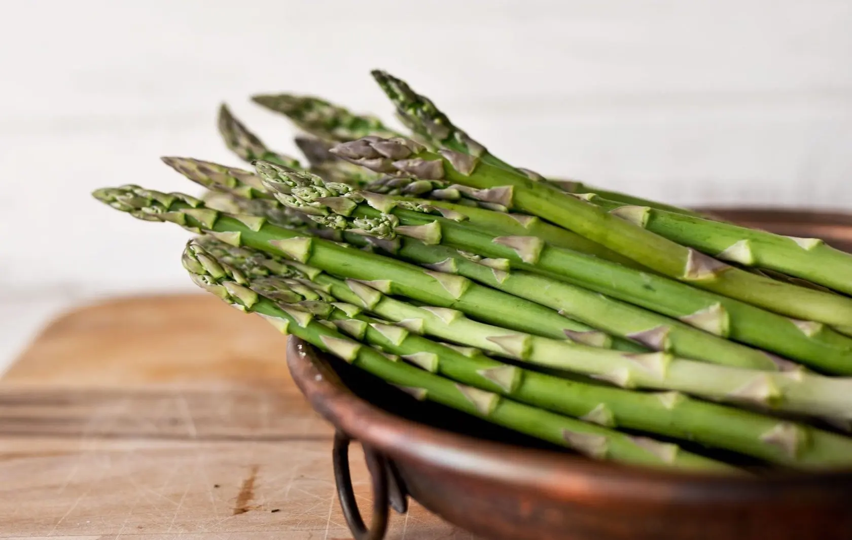 bowl of asparagus on brown wooden chopping board