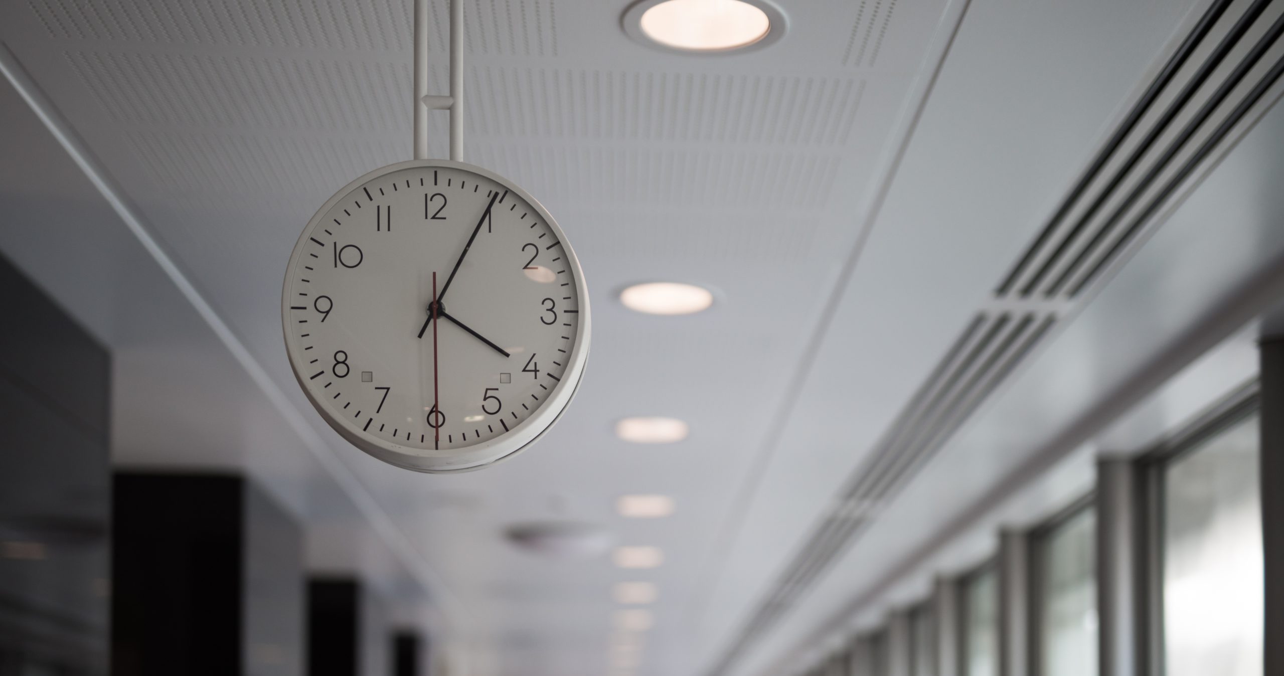 Image of a clock suspeded from the cieling in a white office 
